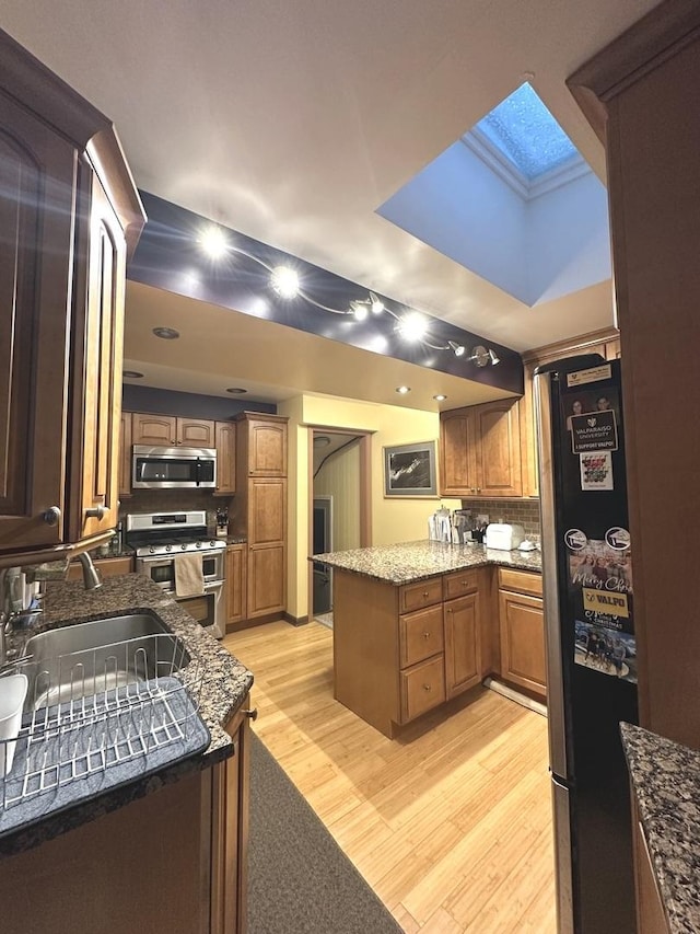 kitchen featuring stone countertops, light wood-style flooring, stainless steel appliances, a peninsula, and a sink