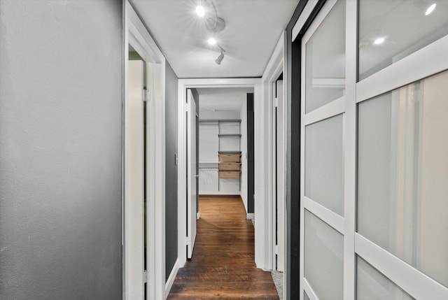 corridor with rail lighting, dark wood-style flooring, and a textured wall