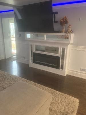 unfurnished living room with dark wood-style flooring, wainscoting, a fireplace, and a decorative wall