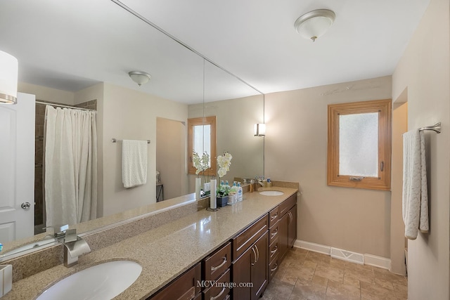 full bathroom featuring double vanity, a shower with curtain, baseboards, and a sink