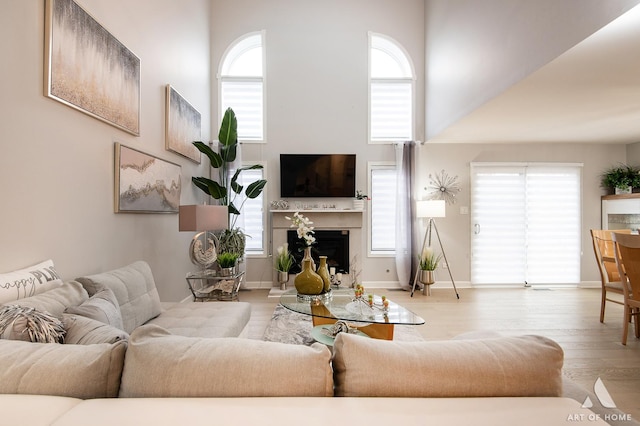 living area with a towering ceiling, a fireplace, baseboards, and wood finished floors