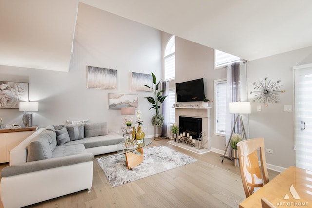 living area with a fireplace with raised hearth, a towering ceiling, baseboards, and wood finished floors