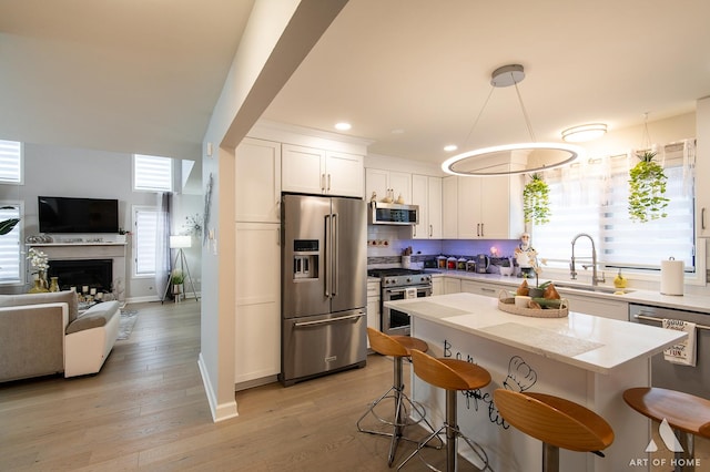 kitchen featuring high end appliances, open floor plan, white cabinetry, a sink, and a kitchen bar