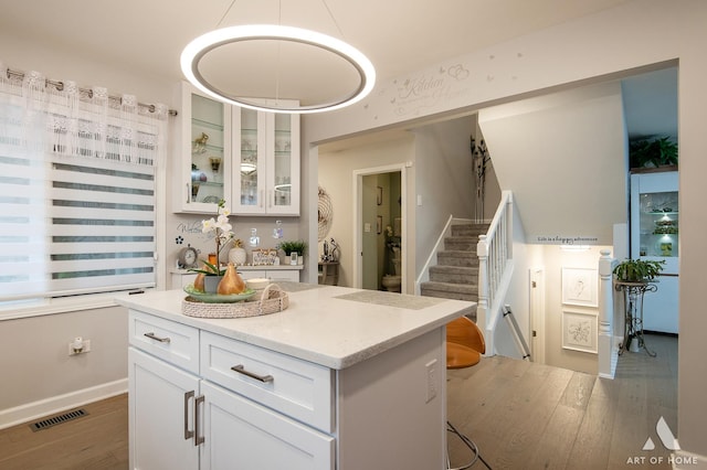 kitchen with visible vents, glass insert cabinets, wood finished floors, a center island, and white cabinetry