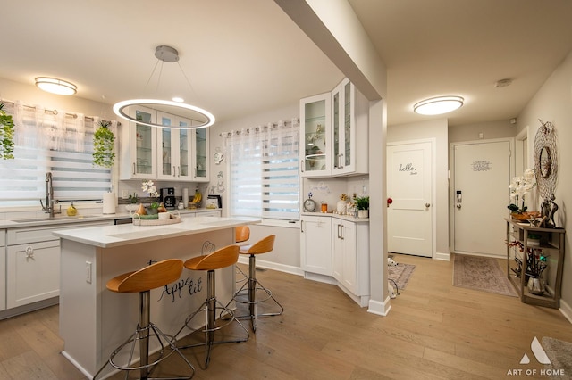 kitchen featuring white cabinets, light wood-style flooring, light countertops, a kitchen bar, and a sink