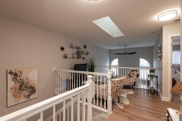 hallway with a skylight, visible vents, an upstairs landing, baseboards, and light wood finished floors