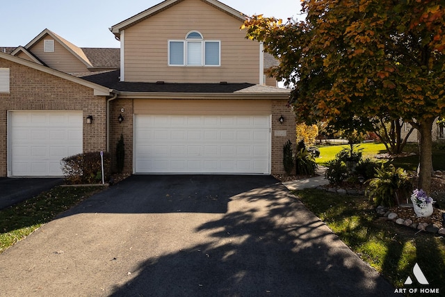 traditional home with driveway, a shingled roof, an attached garage, and brick siding