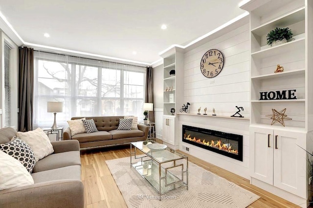 living area with light wood-type flooring, plenty of natural light, crown molding, and a glass covered fireplace