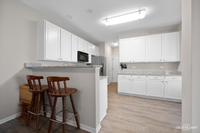 kitchen featuring freestanding refrigerator, white cabinets, a breakfast bar area, black microwave, and light stone countertops