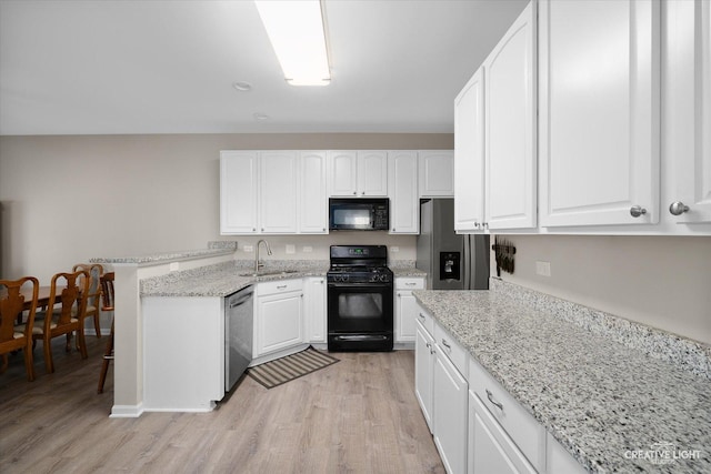 kitchen featuring black appliances, a sink, white cabinetry, light wood-style floors, and a peninsula