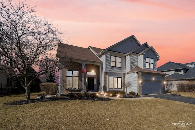 traditional-style home with a garage, a front lawn, aphalt driveway, and brick siding