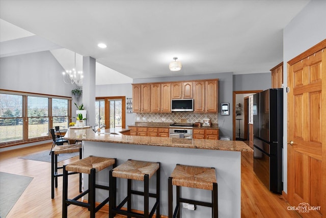 kitchen featuring tasteful backsplash, appliances with stainless steel finishes, stone counters, light wood-style floors, and a kitchen bar