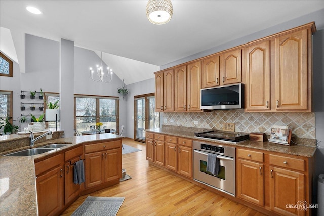 kitchen featuring tasteful backsplash, lofted ceiling, appliances with stainless steel finishes, light wood-style floors, and a sink