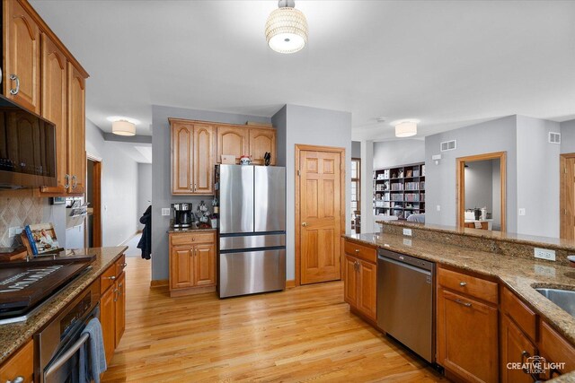 kitchen featuring visible vents, appliances with stainless steel finishes, stone countertops, and light wood-style flooring