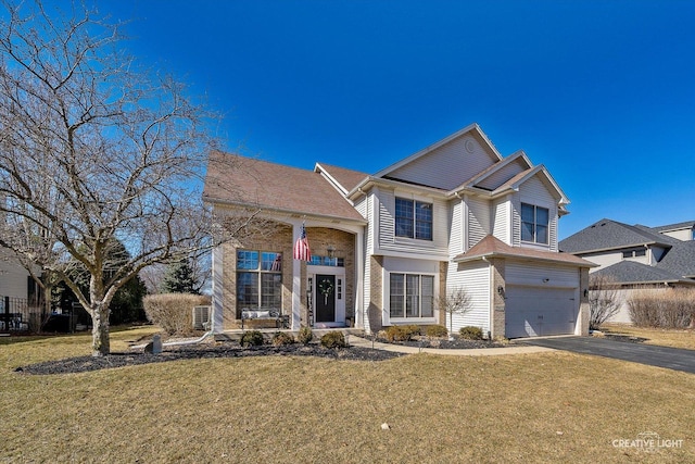 traditional-style house featuring aphalt driveway, a front yard, brick siding, and a garage