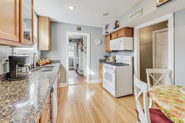 kitchen featuring light stone counters, white appliances, a sink, visible vents, and light wood finished floors