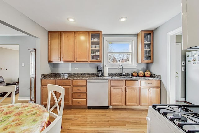 kitchen with light wood-type flooring, white appliances, dark stone countertops, and a sink