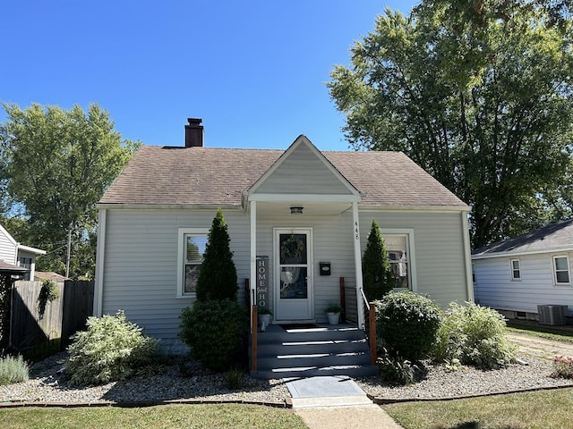 view of front of home featuring central AC, a shingled roof, a chimney, and fence