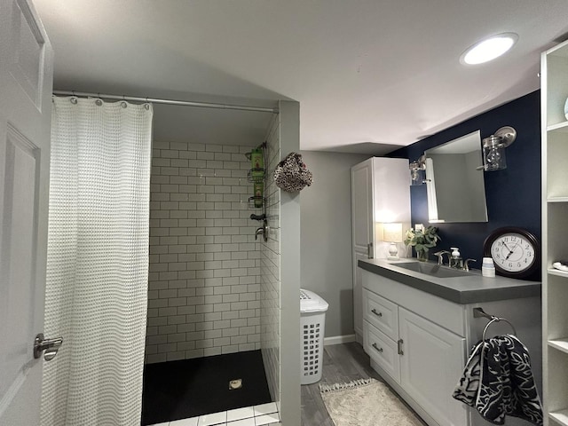 bathroom with wood finished floors, tiled shower, and vanity