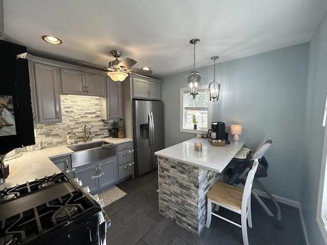 kitchen featuring a breakfast bar area, gray cabinetry, a sink, stainless steel refrigerator with ice dispenser, and black gas range oven