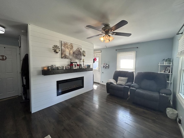 living area featuring dark wood-style floors, a glass covered fireplace, ceiling fan, and baseboards