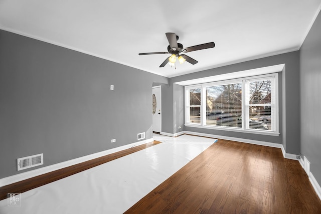 spare room featuring visible vents, crown molding, baseboards, and wood finished floors