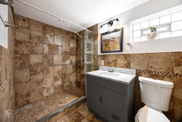 bathroom featuring toilet, a stall shower, vanity, and tile walls