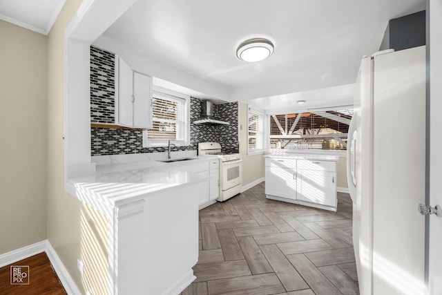 kitchen with white appliances, a sink, white cabinetry, wall chimney exhaust hood, and tasteful backsplash