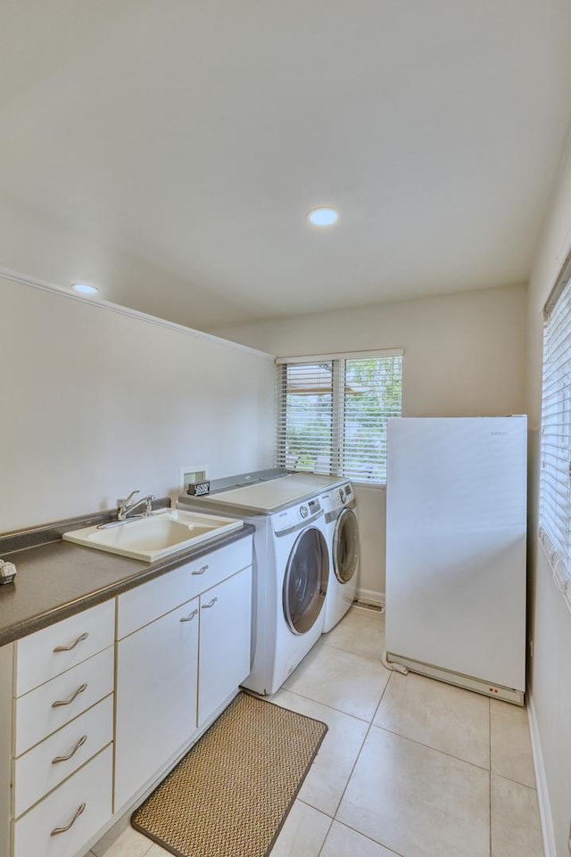 laundry area featuring light tile patterned flooring, washing machine and dryer, a sink, baseboards, and cabinet space