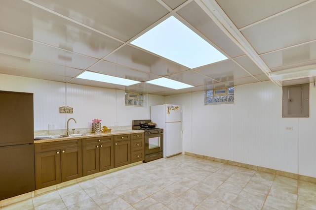 kitchen with brown cabinetry, gas stove, a sink, and freestanding refrigerator