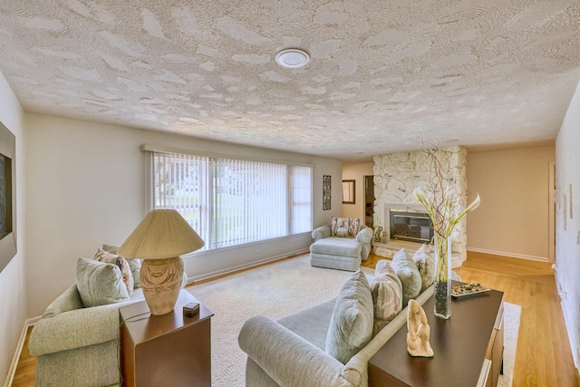 living area featuring a textured ceiling, a fireplace, wood finished floors, and baseboards