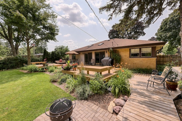 rear view of house featuring brick siding, a lawn, an outdoor fire pit, fence, and a deck