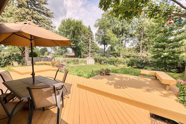 deck with a fenced backyard, a yard, a shed, an outdoor structure, and outdoor dining space