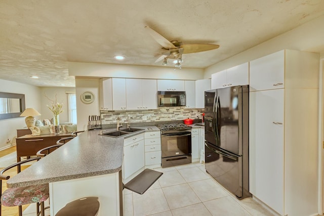 kitchen with decorative backsplash, a peninsula, black appliances, white cabinetry, and a sink