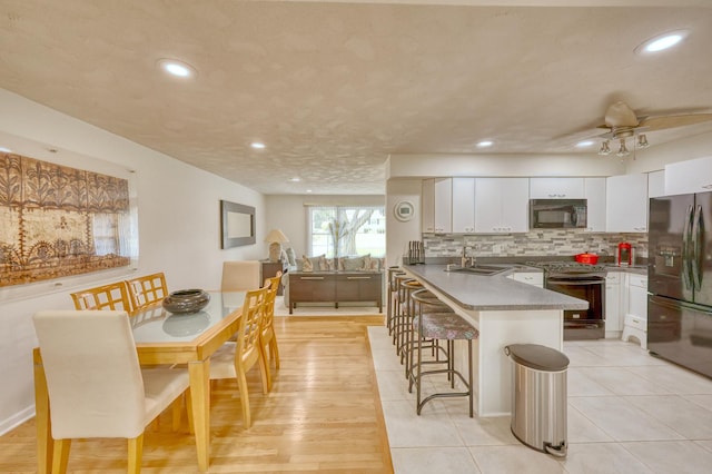 kitchen featuring backsplash, white cabinetry, a sink, a peninsula, and black appliances