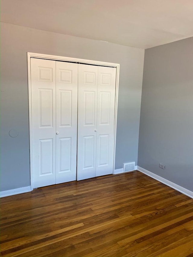 unfurnished bedroom featuring dark wood-type flooring, a closet, visible vents, and baseboards