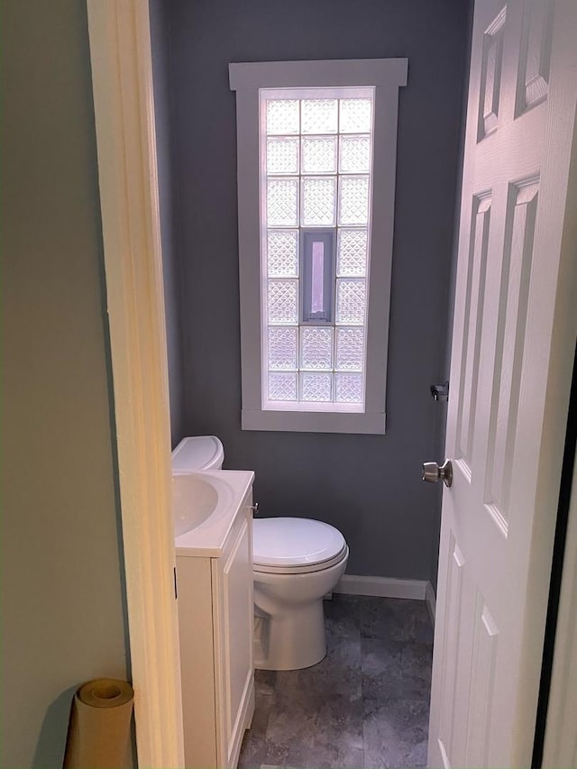 half bath with baseboards, vanity, and toilet