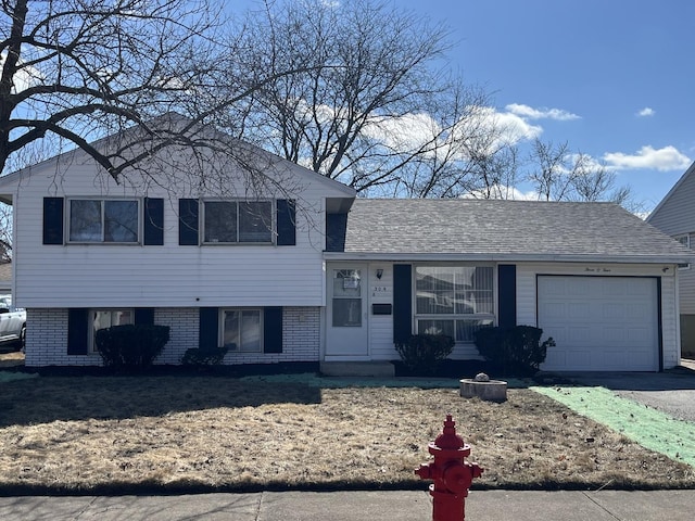 split level home featuring a shingled roof, brick siding, driveway, and an attached garage