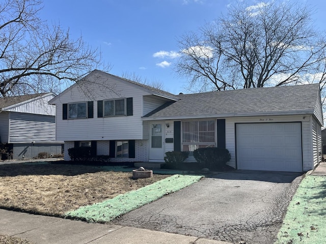 split level home featuring a garage, brick siding, driveway, and a shingled roof