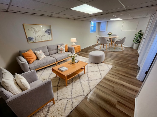 living room featuring a drop ceiling, baseboards, and wood finished floors