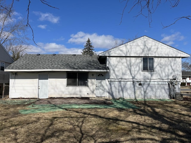 rear view of house with a yard, central AC unit, and roof with shingles