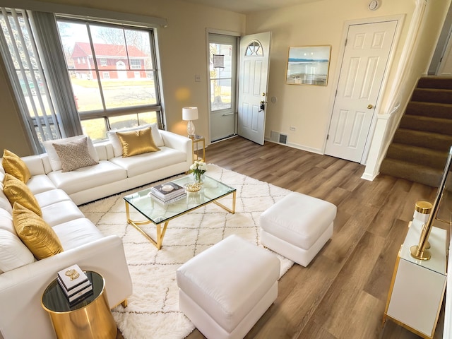 living room with stairs, wood finished floors, visible vents, and baseboards