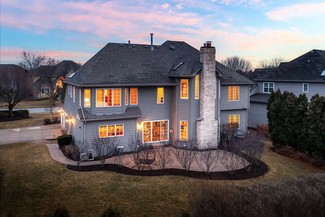 back of house featuring concrete driveway, a yard, a patio area, and a chimney