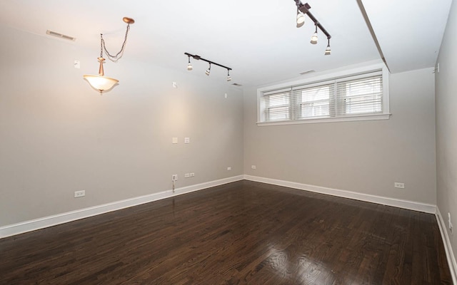 spare room featuring visible vents, track lighting, baseboards, and dark wood-type flooring