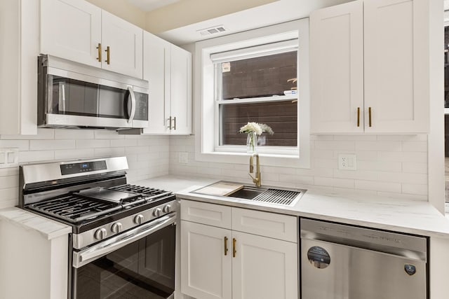 kitchen with backsplash, appliances with stainless steel finishes, white cabinetry, a sink, and light stone countertops