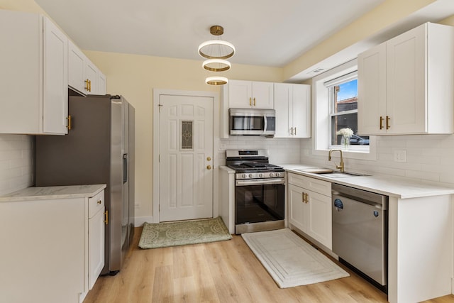 kitchen with stainless steel appliances, light wood-type flooring, white cabinetry, and a sink