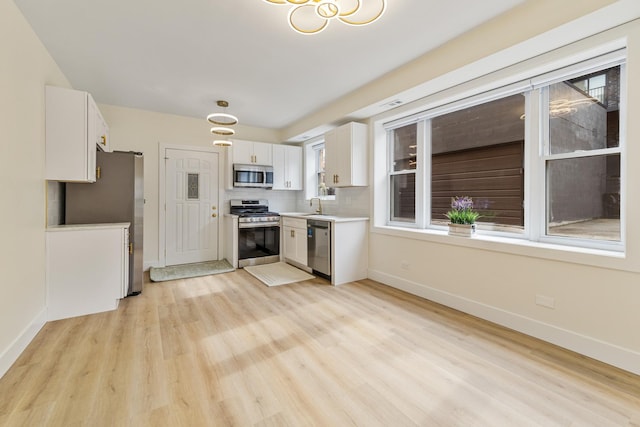 kitchen featuring light wood-style flooring, stainless steel appliances, a sink, white cabinetry, and baseboards