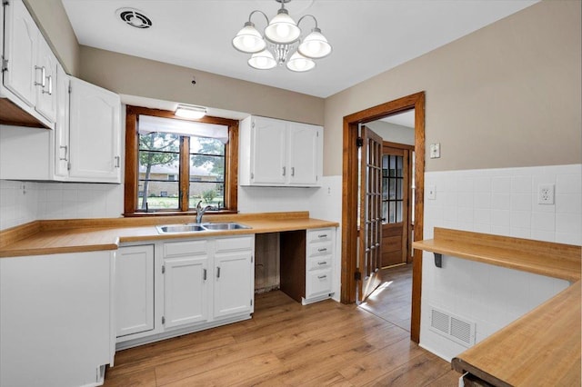 kitchen with a sink, visible vents, white cabinets, light countertops, and light wood finished floors