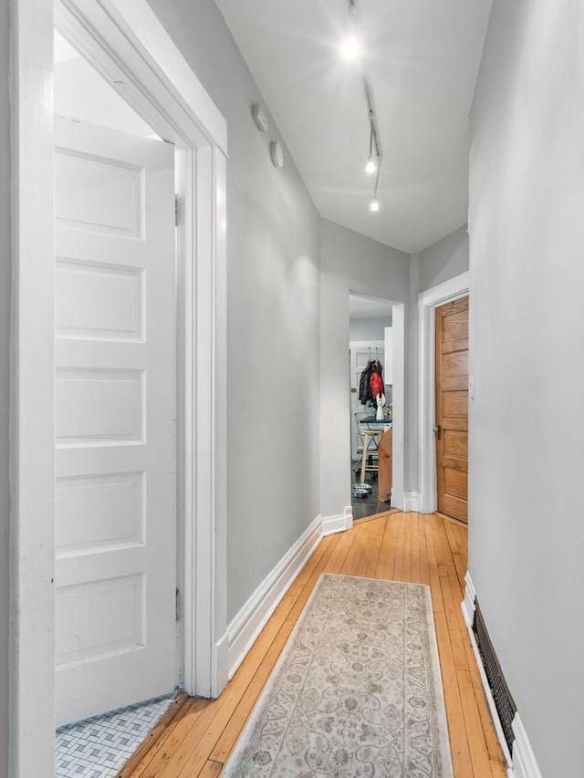 hallway with light wood-type flooring, baseboards, and track lighting