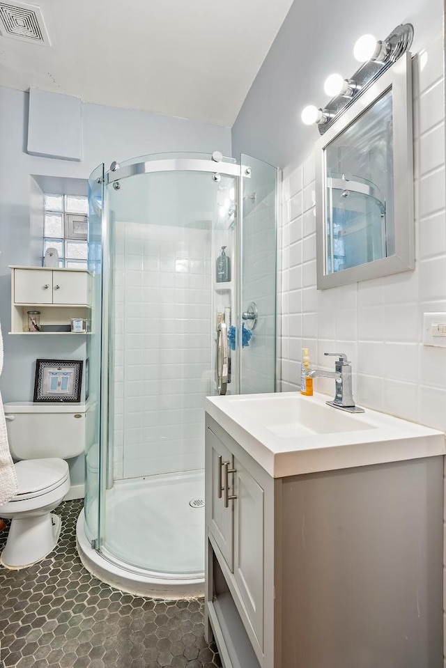 bathroom featuring tile walls, visible vents, toilet, a stall shower, and vanity